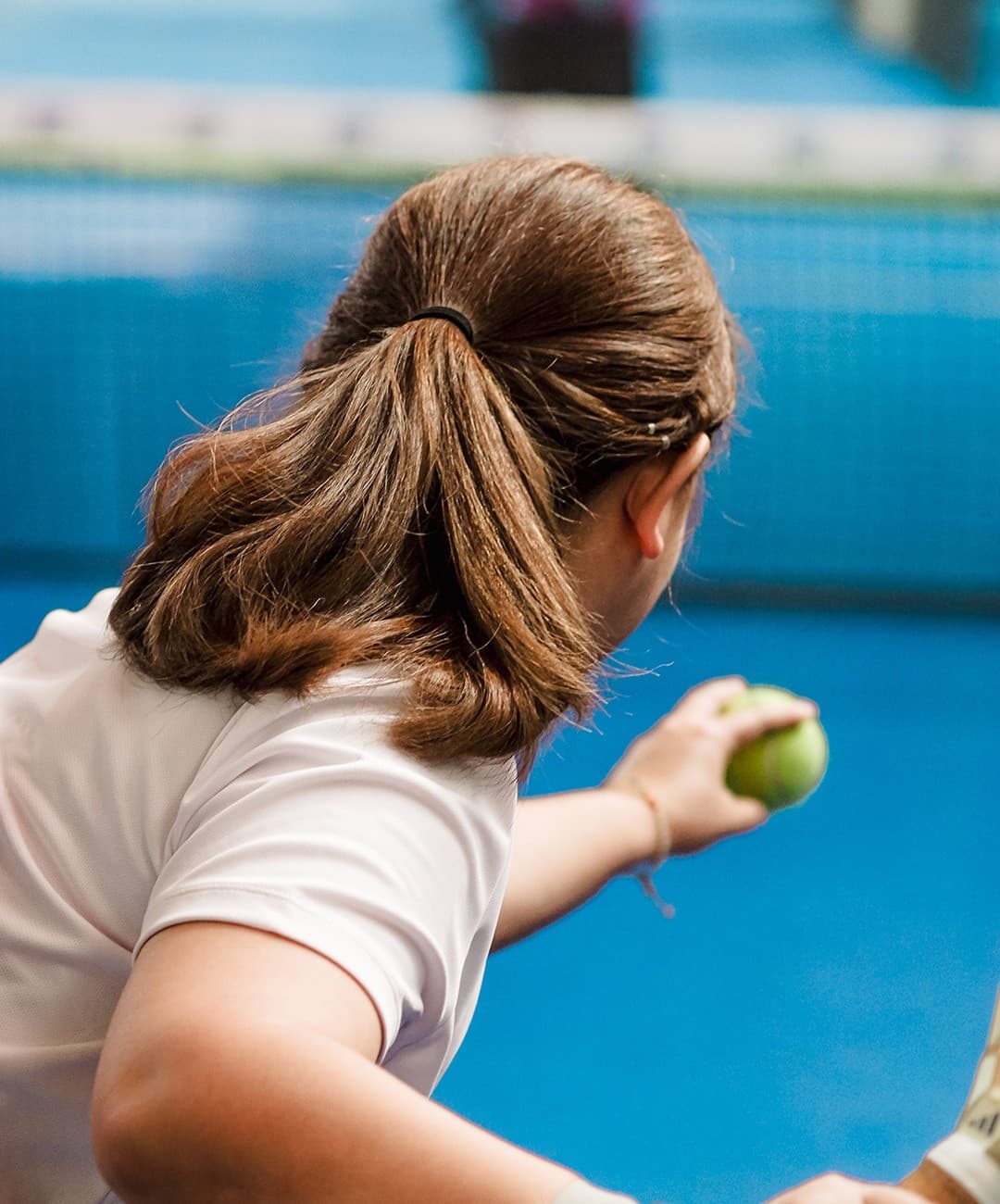 Pemain bersiap servis, close-up rambut kuncir dan bola